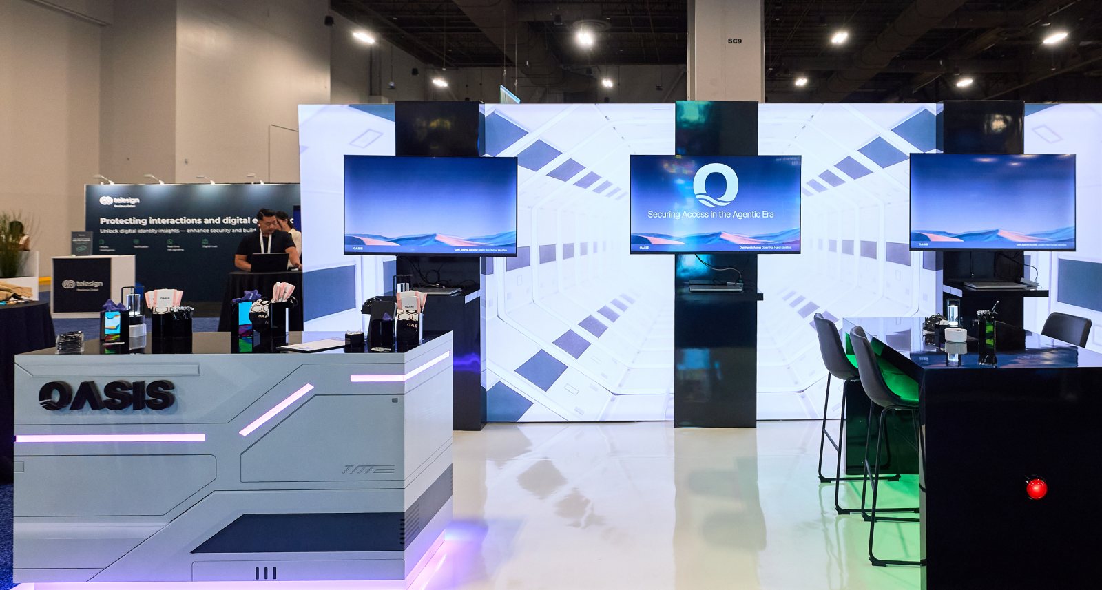 Oasis Security’s conference booth - reception desk, three screens and the white tunnel wall